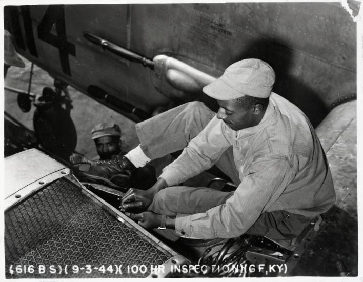 black and white photograph of black man in uniform sitting on a wing and working on an engine