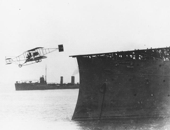 An old photograph of a biplane taking off a boat. 