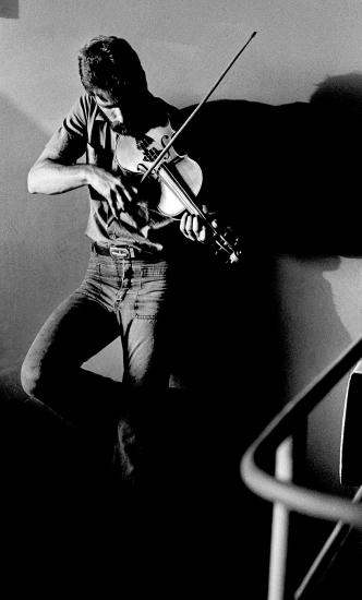 A man playing a violin while leaning on a wall