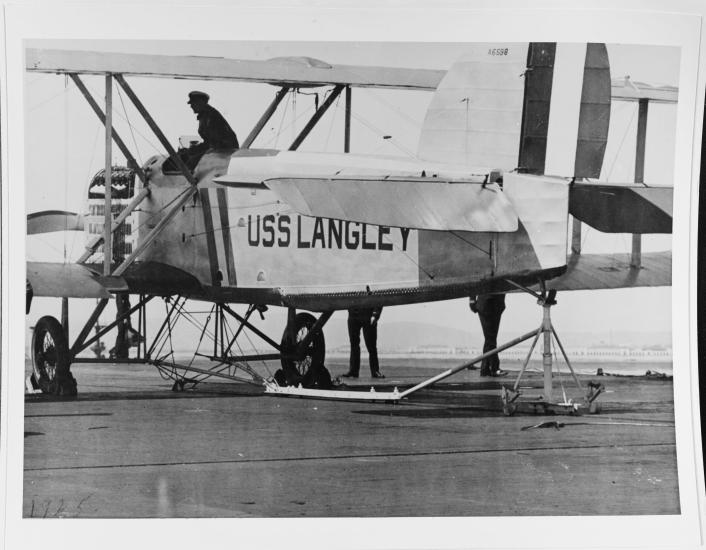 Black and white grainy image of an aircraft with someone sitting on top.