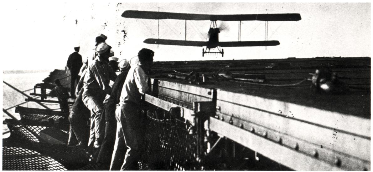 Several individuals lean over a railing watching an airplane land. 