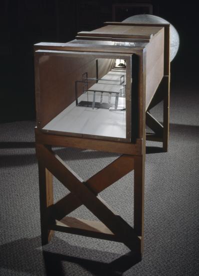 Wooden frame supporting hollow rectangular box-shaped wind tunnel.