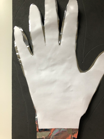 A cut out of a hand on printer paper, stacked on a cut of of a hand on Mylar, on top of a piece of black foam. 