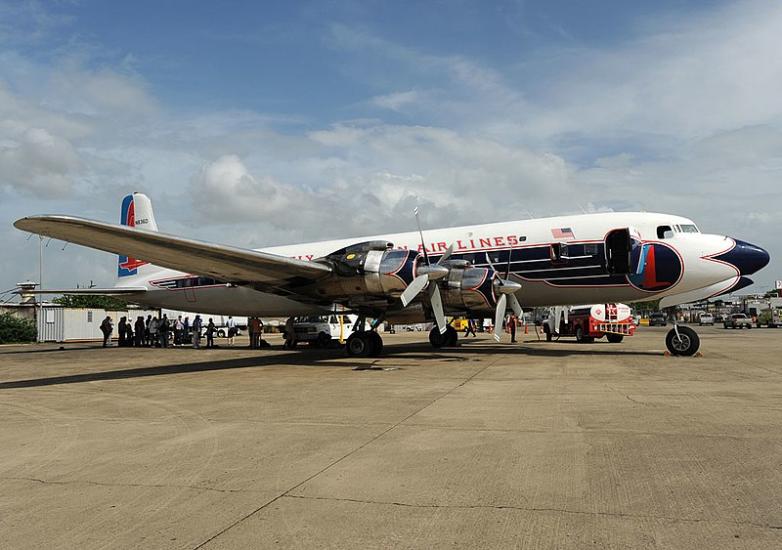 An airplane on a tarmac. The airplane has two silver propellers on the wings. On the body you can read "Air Lines."