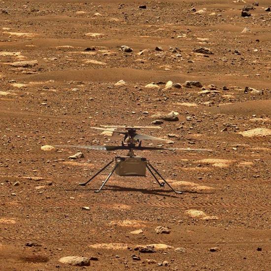 A small helicopter sits at idle on a rocky surface.