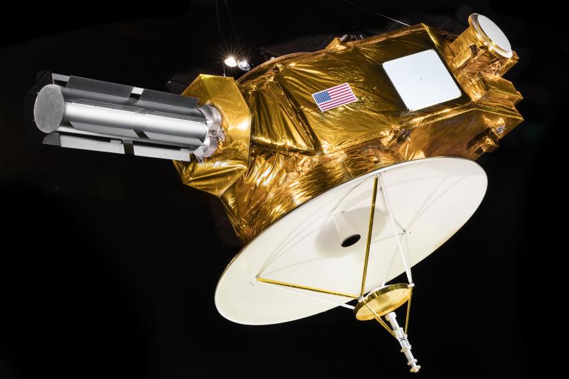 A spacecraft with a round disk on the bottom, a cylinder on the side, and a golden body with the United States flag on it.  