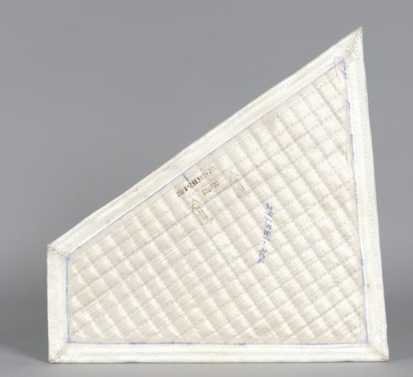 A quadrilateral (four-sided) piece of white quilted fabric. Serial numbers are written on the center of the piece. 