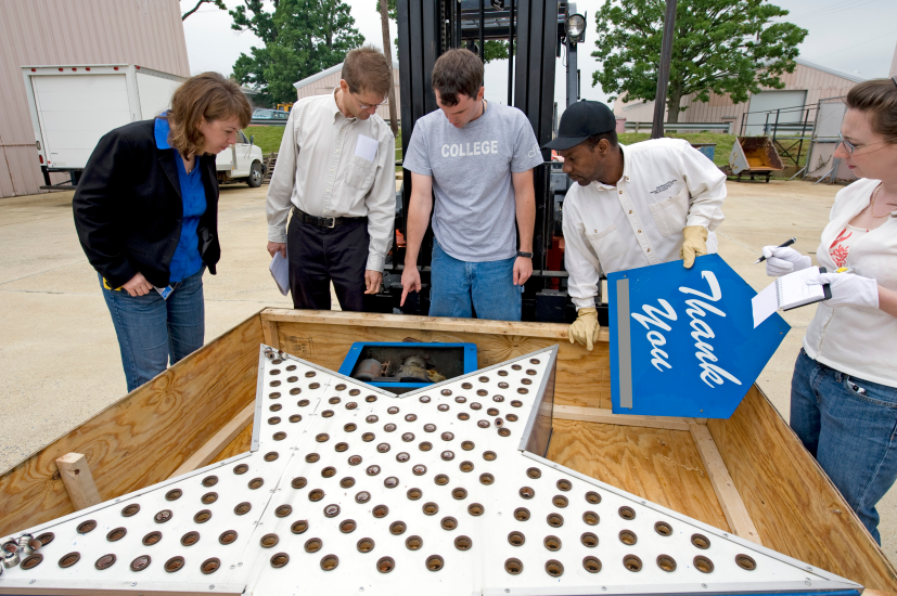 Five people stand around a crate containing a large silver star covered in lights.