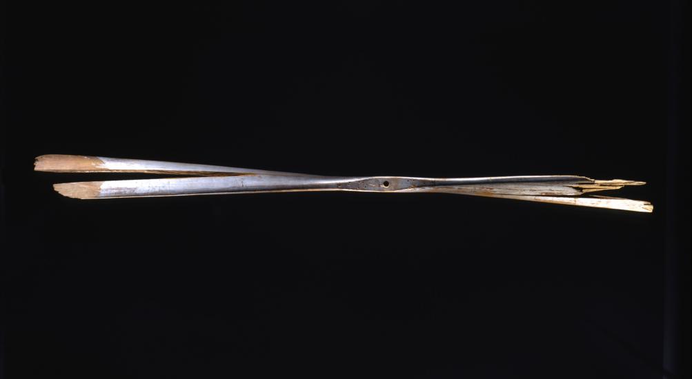 A wooden propeller against a black background. The right side of the propeller is very damaged, and the entire propeller has a split through it.