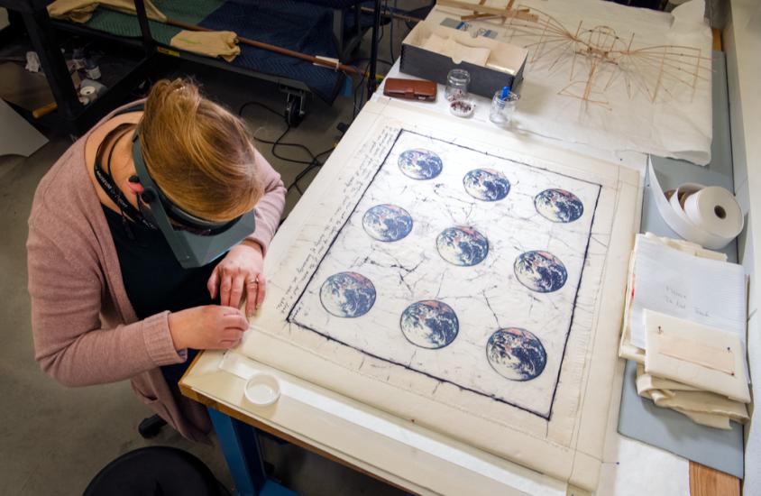 A woman leans over a painting of the Earth conserving it. 