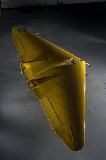 A yellow aircraft that is two wings linked together creating a triangular shape. 