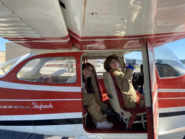 Campers at the S.H.E. Can STEAM Aviation Camp pose in the cockpit of a red, white, and black airplane