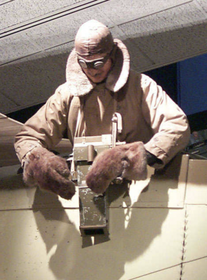 A mannequin leans out of a plane with a camera facing downwards.