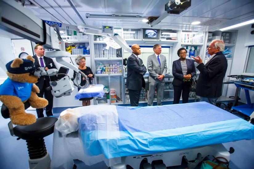 A group of people stand in a semi circle talking inside an operating room.