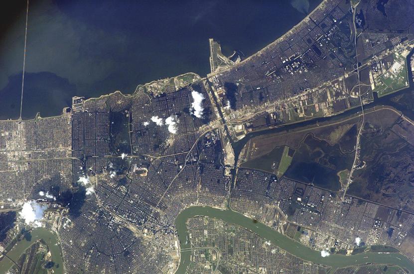 An aerial image of a city on the coast. Large plumes of smoke can be seen as well as extensive flooding.