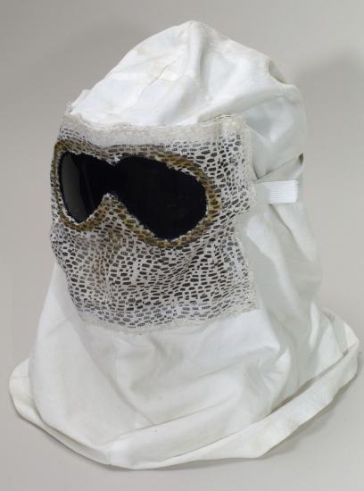 A white hood with goggles propped up for a photograph. The front of the hood has mesh on it, presumably to breathe.