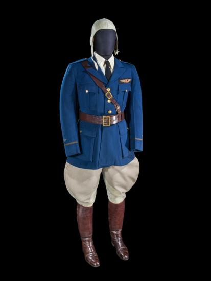 A uniform on a mannequin which includes a deep blue jacket, beige flying hat, beige pants, and tall brown boots.