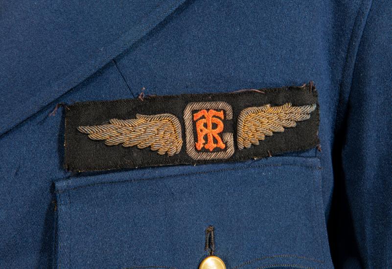 A black patch embroidered with gold wings which have the letter R and T on top of each other at the center.