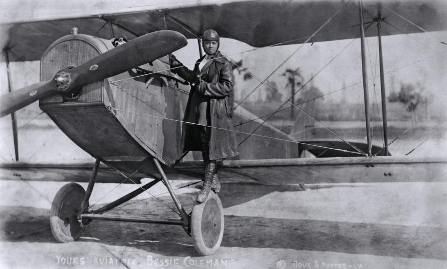 A woman stands on the wing of an airplane.