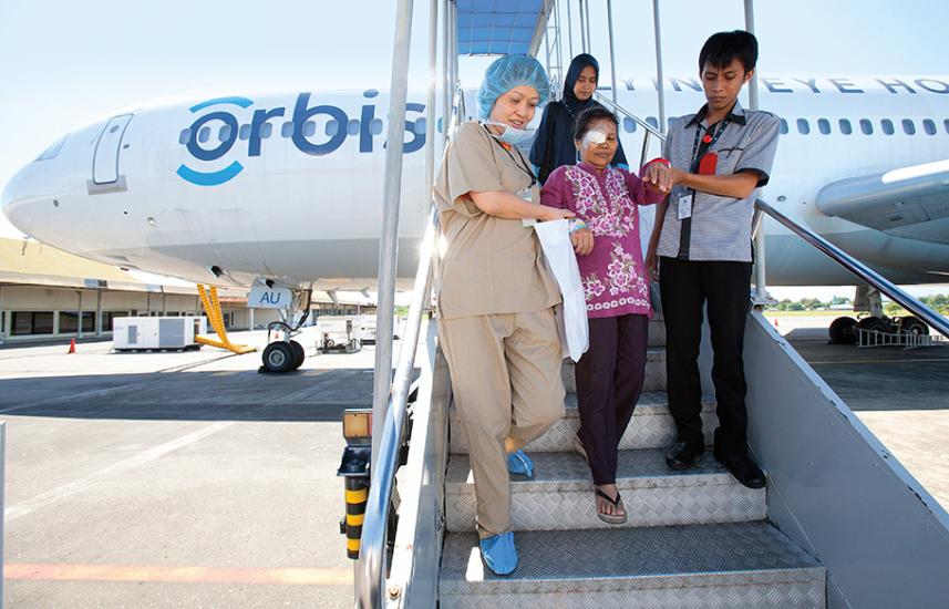 An Indonesian woman wearing a bandage over her eye is escorted off Orbis International’s iconic flying teaching hospital after receiving cataract surgery.