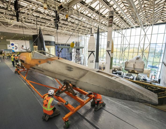 Two workers in a construction vest and helmet adjusts the Star Wars X-wing on its transport device.