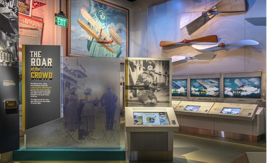 An image from inside the early flight exhibit. A panel says "The Roar of the Crowd" and there is a photo of Harriet Quimby. Propellers are hung on the wall.