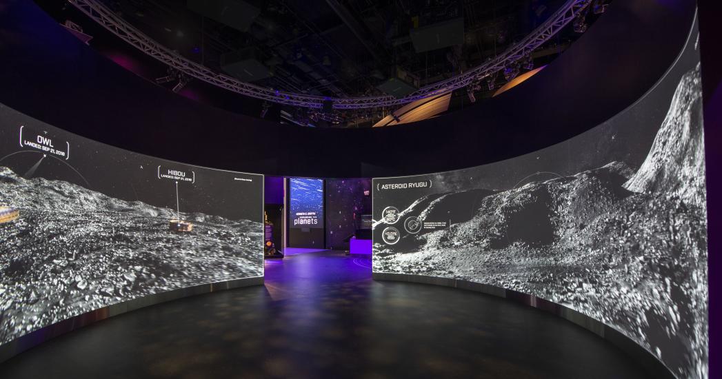 Two large curved screens showing the surface of an asteroid.