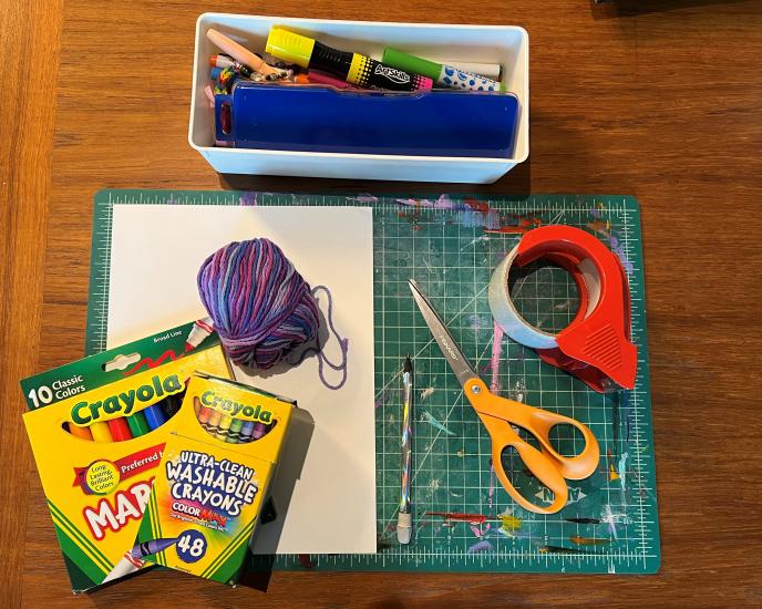 A scissor, tape, markers, yarn, paper, markers and other supplies. 