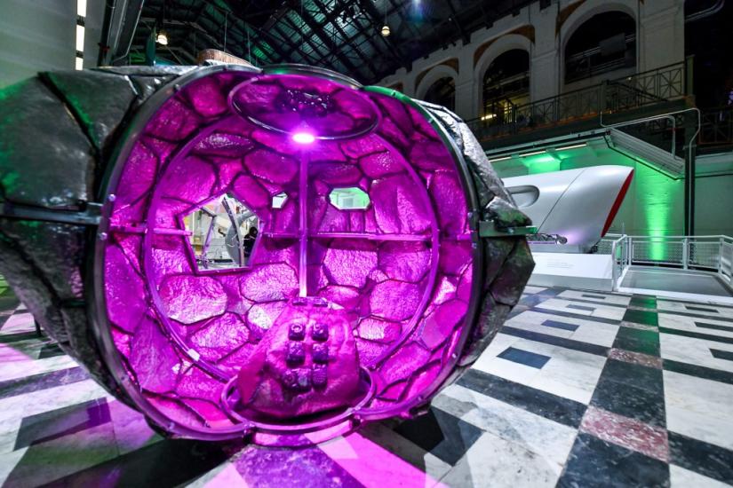 A container shaped like a large rock cut away to review a seating area bathed in purple light on the inside. 