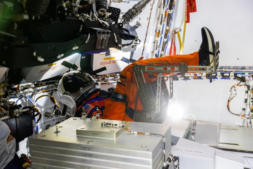 A mannequin wearing an orange spacesuit seated in a spacecraft.