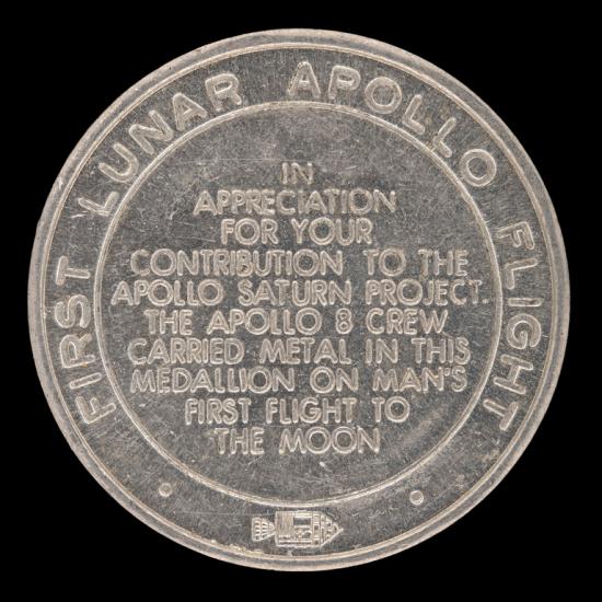 Coin that reads FIRST LUNAR APOLLO FLIGHT; IN APPRECIATION FOR YOUR CONTRIBUTIONS TO THE APOLLO SASTURN PROJECT. THE APOLLO 8 CREW CARRIED METAL IN THIS MEDALLION ON MAN'S FIRST FLIGHT TO THE MOON