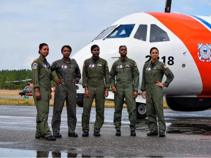 Five black women in flight suits stand in front of an airplane. 