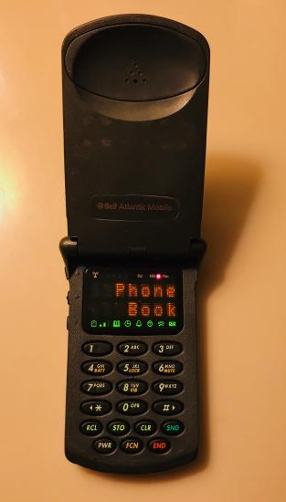 A black flip phone, with a small display screen that read "Phone Book"