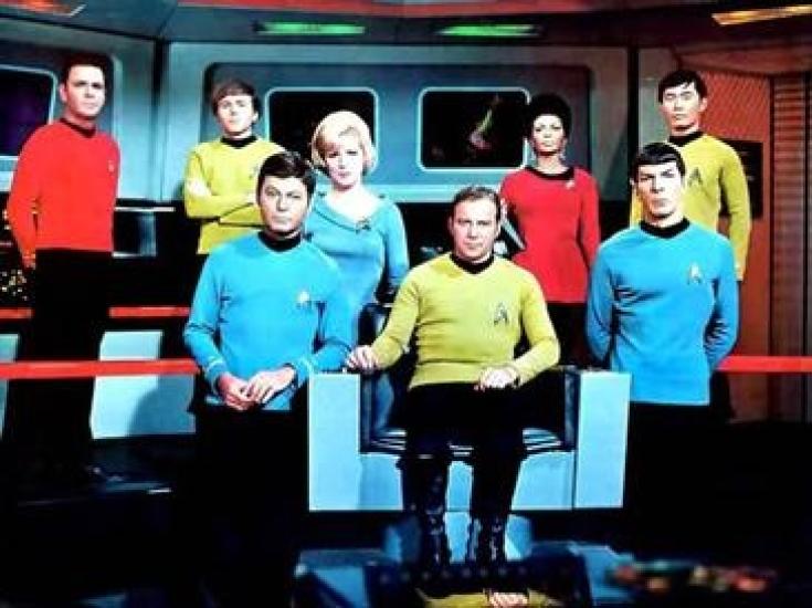 A group of people in primary color uniforms on a spaceship. The people are of different races and genders. 