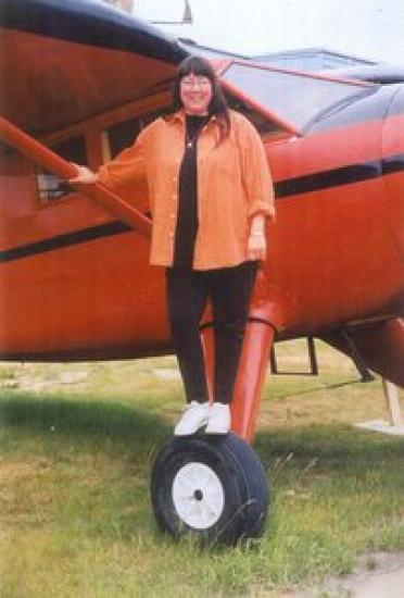 A woman standing by the landing gear of a small aircraft in a field.