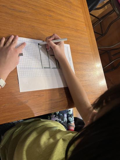 Child writes "Hello" backwards on a piece of paper in large block letters.