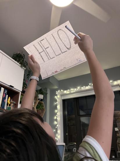 A child holds a piece of paper with "Hello" written on it up to the light.