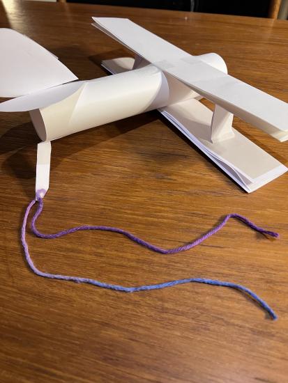 An airplane made out of construction paper with a string tied to the end.