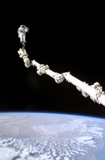 A Remote Manipulator System (Canadarm 2) is pictured in space with an astronaut attached to the end of it.