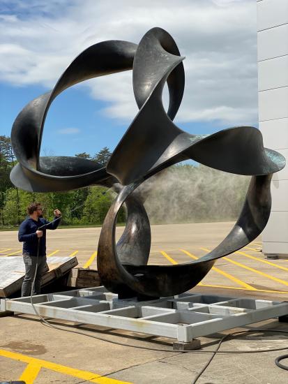 A sculpture with a continuous flow of twists and turns that loop into a symmetrical design is being sprayed by a person.