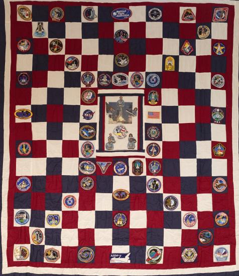 A quilt with red, white, and blue squares and mission patches.