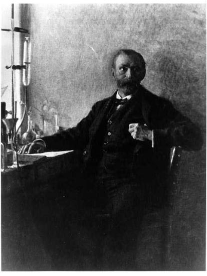 A portrait of a man sitting in a chair at a desk, facing the viewer. 