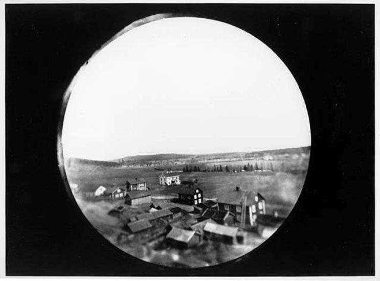 An image of a village from up high. The image itself looks as if it was taken through a peep hole. 