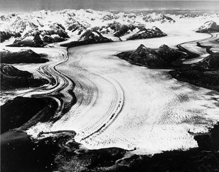 An aerial photograph of what looks to be a white river, but is actually a glacier cutting through the land.