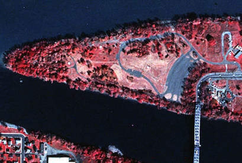 A near infrared aerial photo of a triangular shaped island that has a bridge connecting it to the mainland. The center of the island is a paler red.