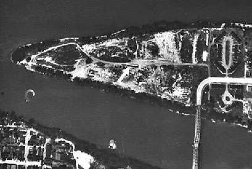 An aerial photo of a triangular shaped island that has a bridge connecting it to the mainland. AN arrow points to a channel in the middle of the island.