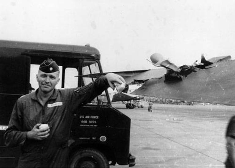 A uniformed man stands leaned up against a van that says U.S. Air Force on the side.