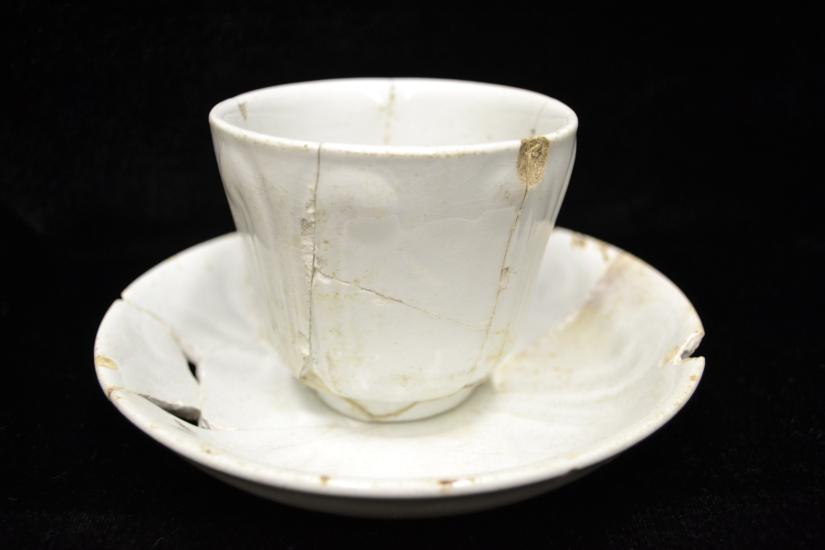 Small white teacup that has cracks in it and has been repaired