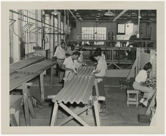 black and white photograph of men and women working on a large piece of corrugated metal