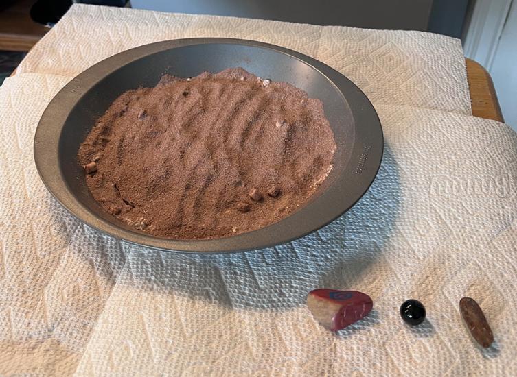 What appears to be dirt or cocoa flour in a pan. The pan sits on paper towels, there are rocks. 